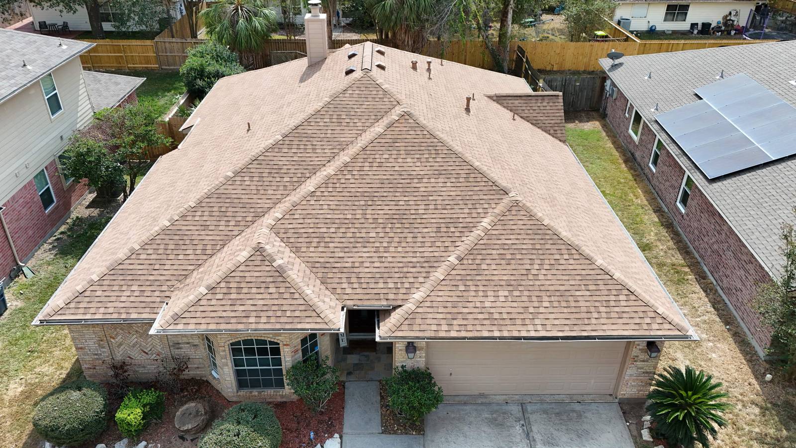 Aerial view of a light tan shingle roof next to darker roofs in a Spring, TX neighborhood