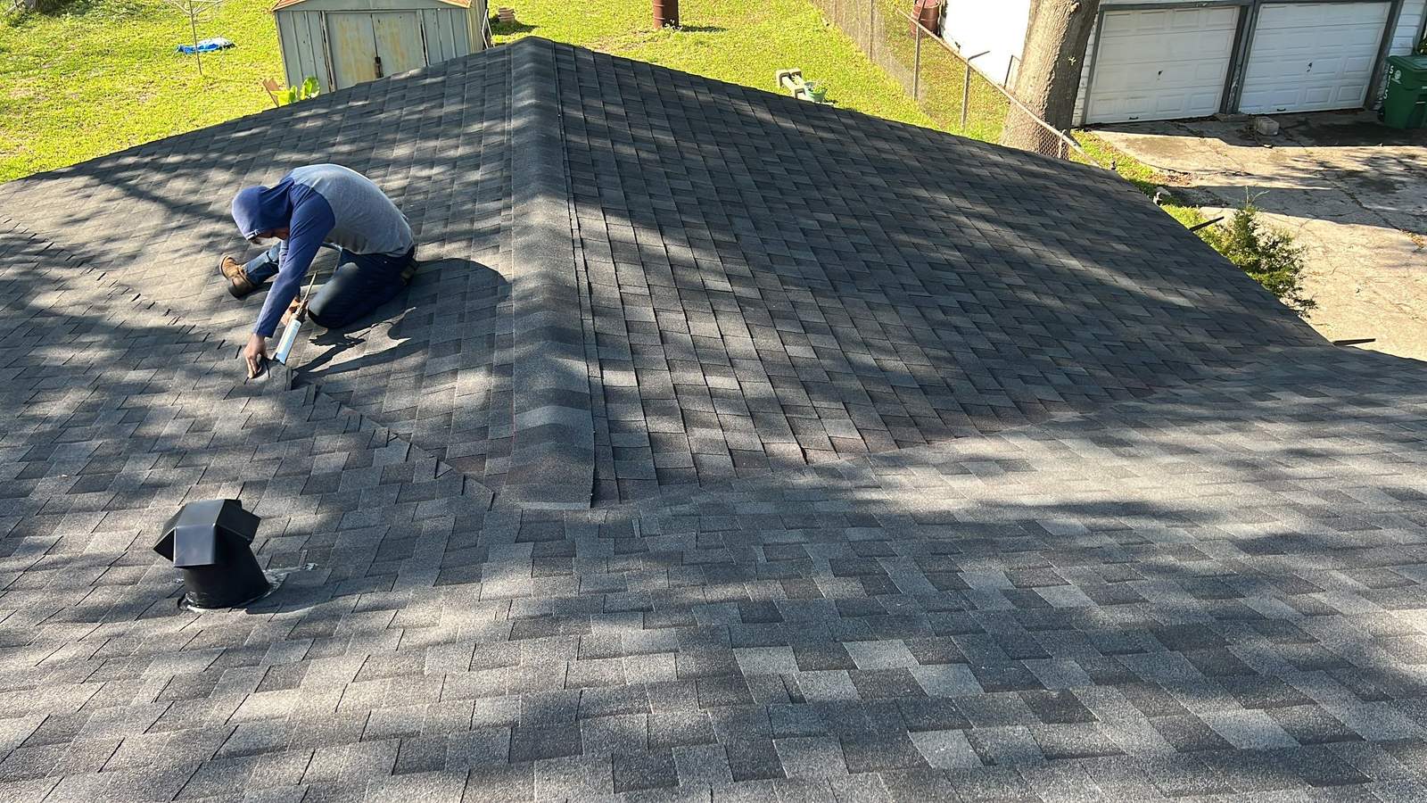 Inspector kneeling to examine shingles up close during a roof inspection