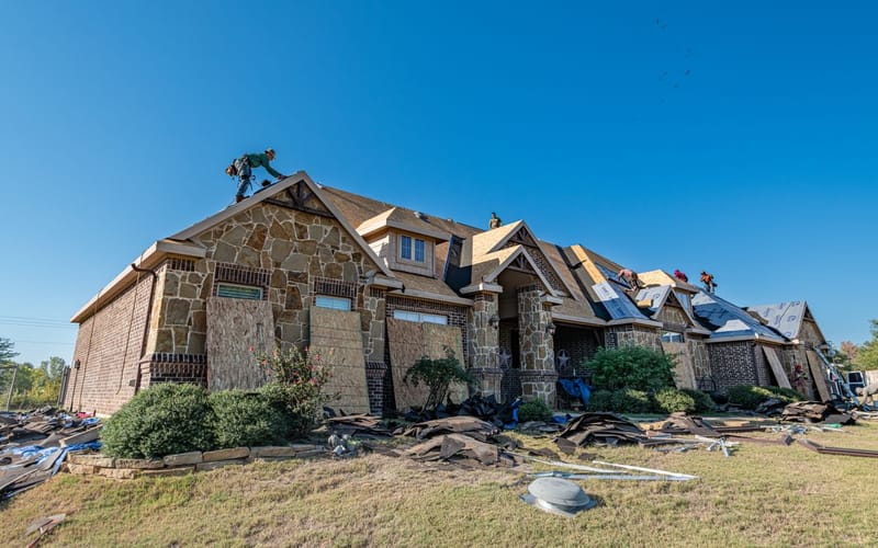 Roof replacement in progress on a Texas home with exposed roof decking and boarded windows