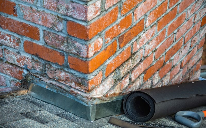 New metal flashing installed around a brick chimney on an asphalt shingle roof